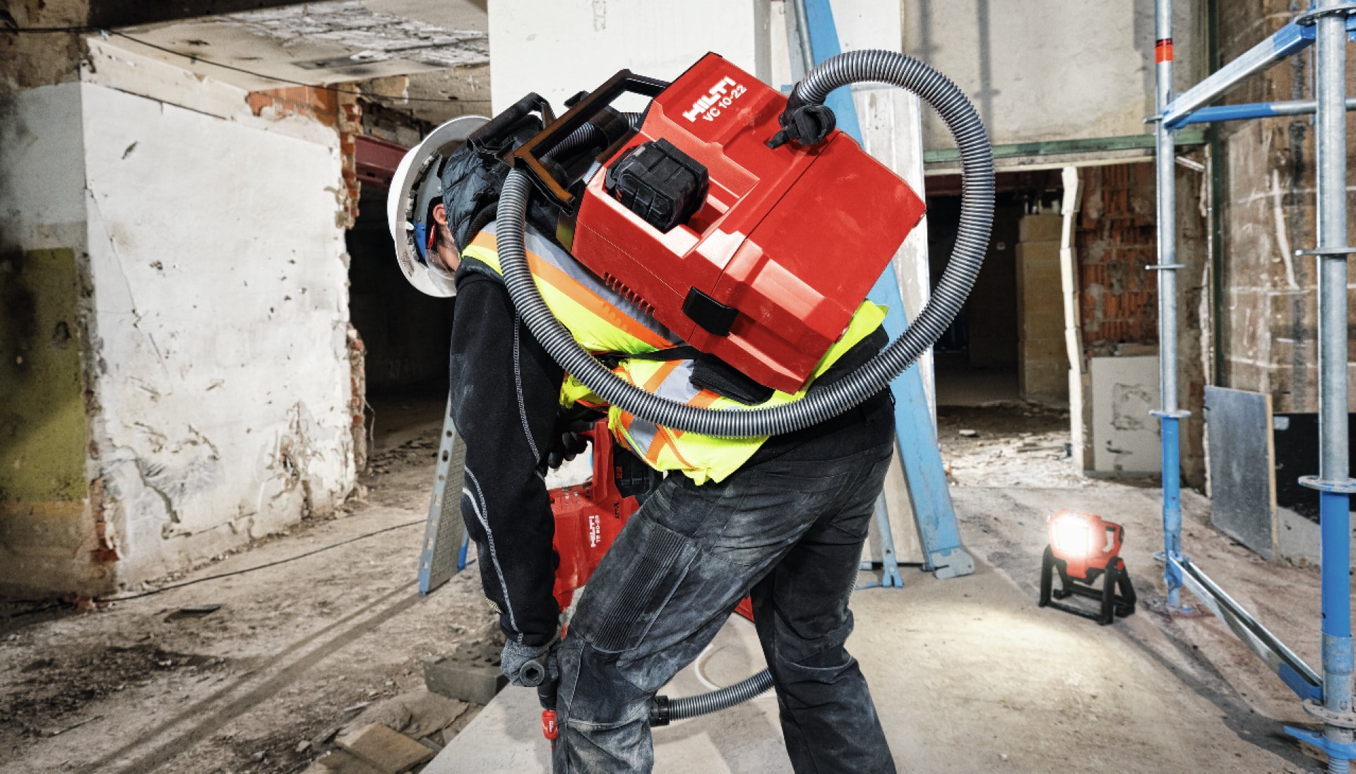 un muncitor utilizează un aspirator pe acumulator pentru a îndepărta praful rezultat din lucrările de demolare